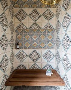 a wooden bench sitting in front of a wall covered in tiles and geometric designs on it