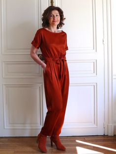 a woman standing in front of a white wall with her hands on her hips, wearing a red jumpsuit