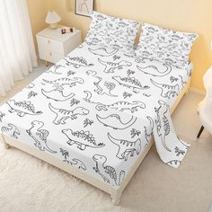 a white bed with dinosaurs on it in a room next to a nightstand and window