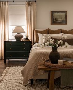 a bedroom with a bed, nightstands and flowers on the table in front of it