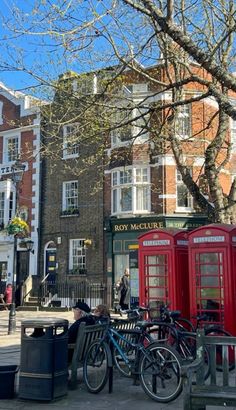 two red telephone booths sitting next to each other on a sidewalk near tall brick buildings