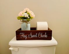 a wooden sign that says hey sweet cheeks sits on top of a toilet with flowers