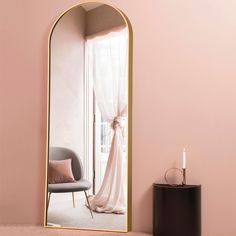 a pink room with a large mirror and chair next to the window that has curtains on it