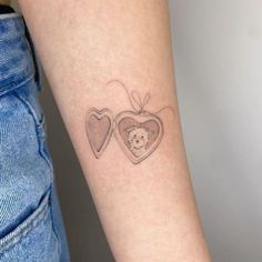 two hearts and a teddy bear tattoo on the left inner arm, with a small heart in the middle