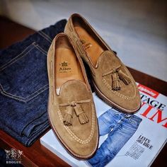 a pair of tan suede shoes sitting on top of a wooden table next to jeans