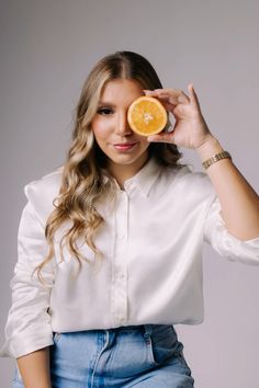 a woman is holding an orange in front of her face and looking at the camera