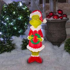 the grinch statue is standing in the snow next to christmas trees and potted plants