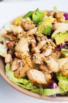 a salad with chicken, lettuce and dressing in a bowl on a table