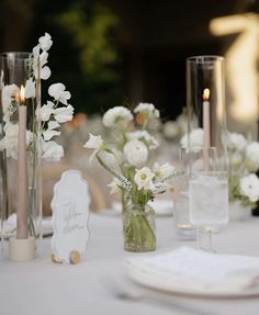 the table is set with white flowers in vases, candles and napkins on it