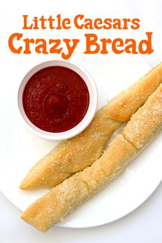 two long bread sticks on a plate with ketchup and sauce in a bowl