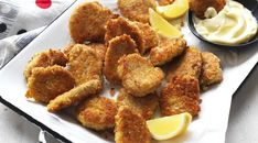 some fried food on a white plate with lemon wedges and mayonnaise next to it