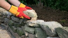 a person in yellow gloves and red mitts is placing rocks on a stone wall