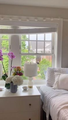 a bed room with a neatly made bed and two vases filled with flowers on top of it