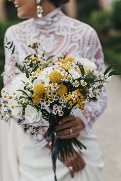 a woman in a white dress holding a bouquet of yellow and white flowers on her wedding day