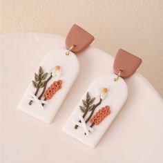 two white and orange earrings with flowers on them sitting on a table next to a wall