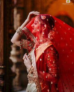 a woman in a red and gold bridal outfit with her hands on her head