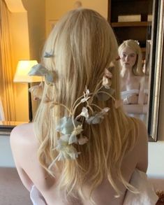 a woman with long blonde hair and flowers in her hair is looking at herself in the mirror