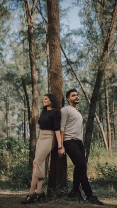 a man and woman standing next to each other in front of a tree with their arms around each other