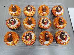 twelve cupcakes decorated like turkeys with leaves and sprinkles in a plastic container