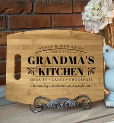 a wooden cutting board with the words grandma's kitchen on it next to flowers