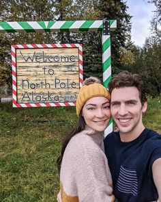 a man and woman pose in front of a welcome sign for north pole alaska,