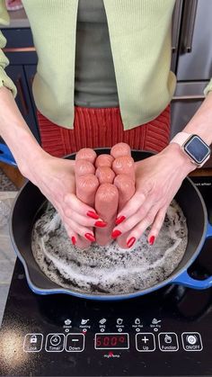 a woman is cooking hot dogs in a frying pan on the stove top with her hands