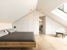 a bed sitting under a window in a bedroom next to a white chair and wooden floor