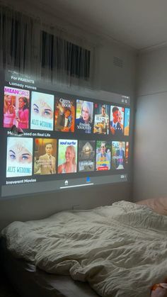 an unmade bed in front of a flat screen tv with many movies on it