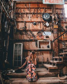 a woman sitting on steps in front of a building with lots of junk hanging from it