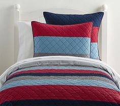 a bed with red, blue and grey bedspread on top of white headboard