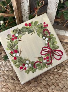 a christmas wreath painted on a canvas with red ribbon and holly berries in the center