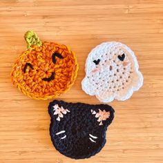 three crocheted pumpkins and a black cat on a wooden surface, one has a ghost face