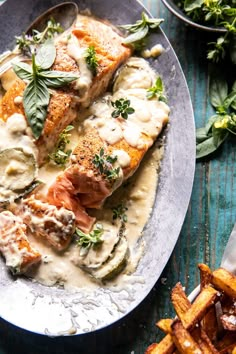 a white plate topped with fish covered in sauce and garnished with green leaves