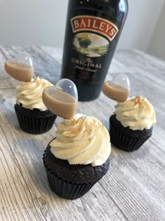 three cupcakes sitting on top of a wooden table next to a bottle of bailey's