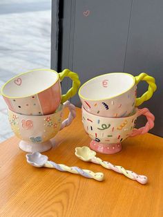 two cups and spoons are sitting on a table next to each other with letters painted on them