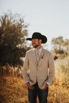 a man wearing a cowboy hat standing in a field with his hands in his pockets