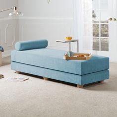 a blue couch sitting on top of a carpeted floor next to a table with a tray