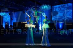 two women dressed in green and white dancing on stage at an event with blue lighting