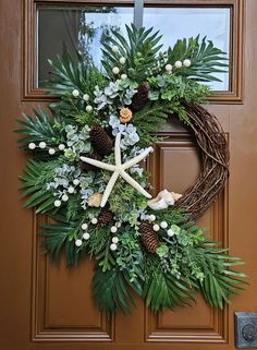 a wreath with starfish, pine cones and greenery is hanging on the front door