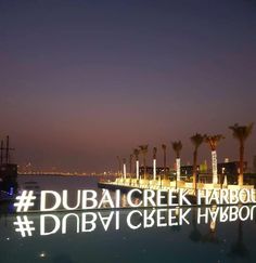 the words dubai creek harbour are lit up at night with palm trees in the background