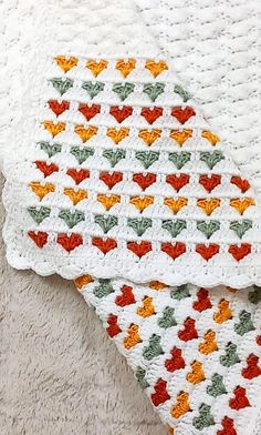 two crocheted blankets are laying next to each other on a white blanket with red, green and yellow leaves