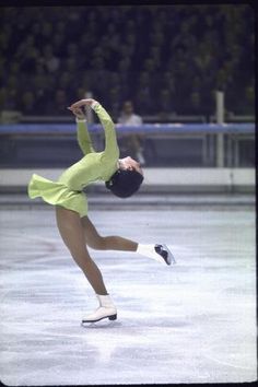 a woman skating on an ice rink wearing a green outfit and white socks, with her arms in the air