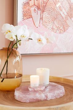 two white candles sitting on top of a table next to a vase with flowers in it