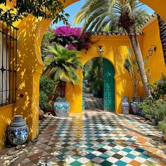 an archway leads into a colorful courtyard with potted plants and palm trees in the foreground