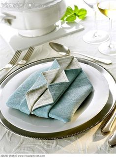 two folded napkins sitting on top of a white plate next to silverware and wine glasses