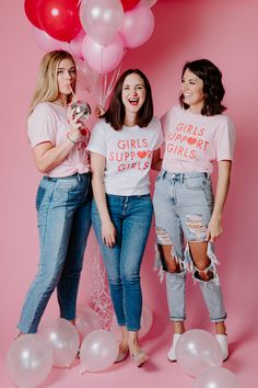 three women standing next to each other with balloons in the air and t - shirts saying girls support girls