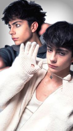 two young men with short hair and white sweaters, one wearing a chain necklace