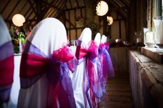 rows of white chairs with purple and red bows on them in a banquet hall setting