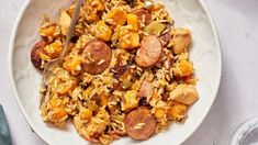 a white bowl filled with rice and sausage next to a fork on top of a table