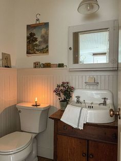 a white toilet sitting next to a sink in a bathroom under a painting on the wall